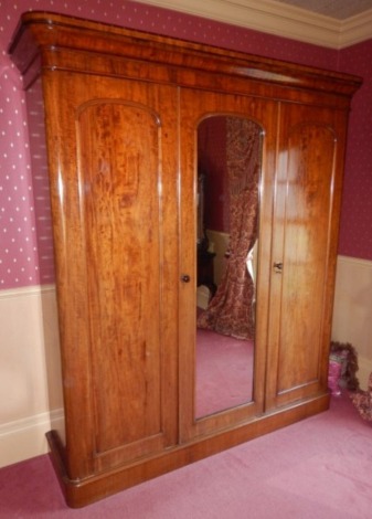 A Victorian mahogany triple wardrobe, the top with a moulded cornice above three doors, the central door with a mirrored panel, enclosing four linen drawers above two short and two further drawers, flanked by an open section for hanging clothes, on a plin