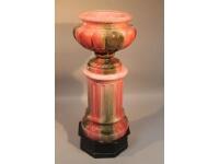 A large 20thC classical style urn decorated in pink and green glaze on round column and wooden base