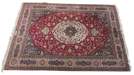 A Kashan red ground rug, decorated with a central cream and blue medallion, with flowers and foliate scrolls within, against a field with further flowers and medallions, within repeating floral and Arabesque medallion borders, 325cm x 225cm.