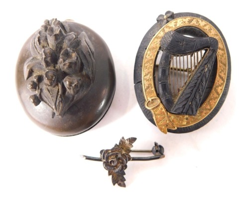 Two carved jet oval brooches, comprising a oval example with yellow metal buckle outer border and central harp, 4cm high, a carved molten lava oval pendant with raised flowers, 4cm high, and a silver rose brooch. (3)