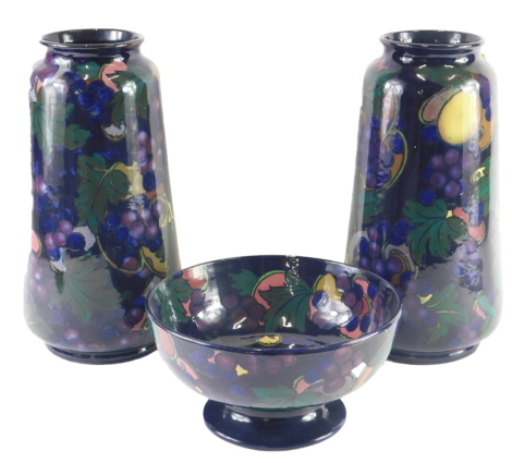 A pair of Royal Stanley Jacobean ware pottery vases, each decorated with fruit and leaves, on a dark navy ground, printed marks to underside, with matching bowl.