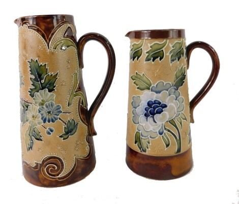 Two Royal Doulton Lambeth stoneware jugs, each with a brown border, on a glazed light brown body with blue flowers, 20cm high. (2)