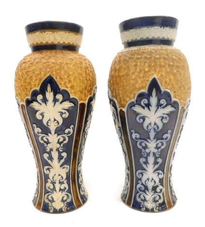 A pair of similar Doulton Lambeth ware vases, each with a blue rim with scroll work body, in raised relief, stamped to underside, 27cm and 28cm high.