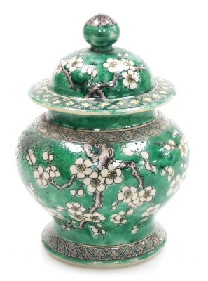 A Quing dynasty porcelain vase and cover, of baluster form, decorated with prunus blossom on a green ground, bears four character Kang-Hsi mark, 15cm high. (AF)