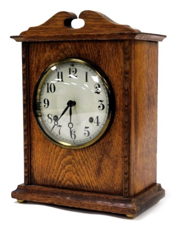 An Edwardian oak cased mantel clock, circular enamel dial bearing Arabic numerals, eight day American movement, New Haven USA, with coil strike, the case of architectural form, raised on brass bun feet, with pendulum and key, 32cm high, 23cm wide.