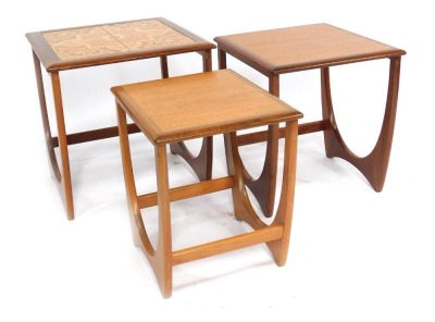 A nest of three G-Plan teak tables, each with a tiled top, raised on U shaped supports, largest 49cm high.