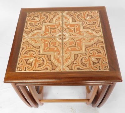 A nest of three G-Plan teak tables, each with a tiled top, raised on U shaped supports, largest 49cm high. - 3