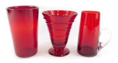 A Whitefriars studio glass ruby red vase, designed by Barnaby Powell, of conical design with raised trailing decoration, on out swept circular foot, pattern number 9296, 14cm high, a Whitefriars ruby glass wave ribbed glass, numbered 8473, 15cm high, and