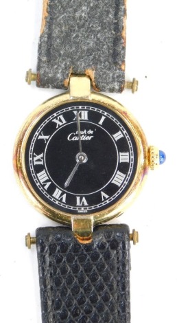 A Must de Cartier lady's wristwatch, with a black Roman numeric face with silver hands, in a silver gilt outer case, white metal stamped 925, and numbered 18 081333, with blue winder, on worn black leather strap, lacking clasp, 16.1g all in.