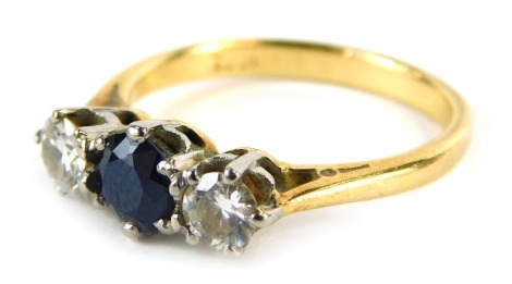 An 18ct gold sapphire and diamond three stone dress ring, the central round brilliant cut sapphire in claw setting, being 5mm x 5mm x 3.88mm, flanked by two diamonds, 3.8mm x 3.8mm x 3.4mm, each approx 0.25ct, in platinum claw setting, on a yellow metal b