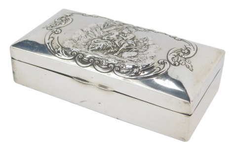 A late Victorian silver cigarette box, of rectangular form, the hinged lid embossed with a scene depicting male and female in 18thC dress, in rural scenes surrounded by scrolls, enclosing a treen interior, Birmingham 1899, 15.5cm wide.