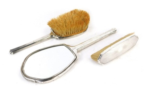 A George VI silver mounted dressing table set, comprising hand mirror, hair brush and clothes brush, each piece with engine turned decoration, Birmingham 1944.