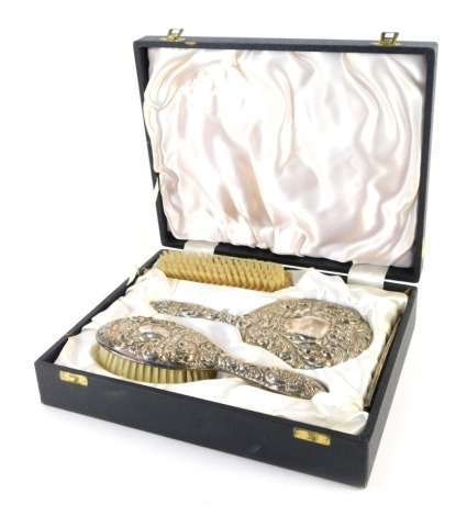 An Elizabeth II silver four piece dressing table set, comprising hand mirror, hair brush, clothes brush and comb, repousse decorated with foliate motif, swirls, leaves, and figural face of a man, Birmingham 1977, in presentation case.