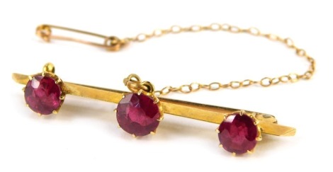 A bar brooch, set with three dark red stones, each in claw setting, on a single pin back with safety chain, yellow metal unmarked, 4cm wide, 3.8g all in.