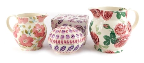 A group of Emma Bridgewater pottery, comprising a trinket box and cover decorated in the Egg and Feather pattern, of egg form, 14cm wide, boxed, together with a 1½ pint jug, decorated in the Pink Hellebore pattern, 14.5cm high, and a 3 pint jug decorated 