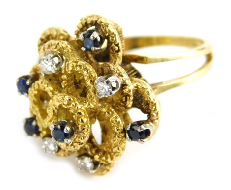 A Kutchinsky modern design dress ring, formed as layers of bark effect swirls, set with sapphires and diamonds, on V splayed shoulders, yellow metal unmarked, size S, 16.1g all in.