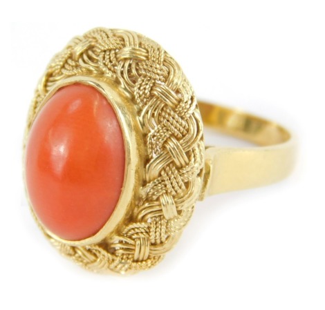 A Kutchinsky coral dress ring, the oval coral in rub over setting with outer woven design border, on a plain band, stamped 18k, ring size N, 6.7g all in.