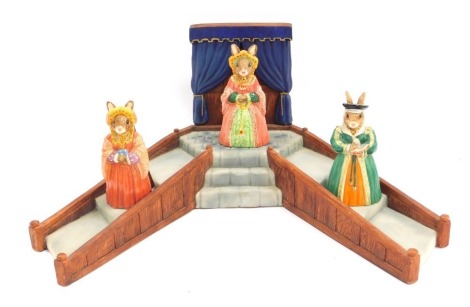 Three Royal Doulton Bunnykins figures from The Tudor Collection, comprising Jane Seymour DB308, Catherine of Aragon DB306, and Catherine Parr DB311, together with a resin stand, 40cm wide. (4)