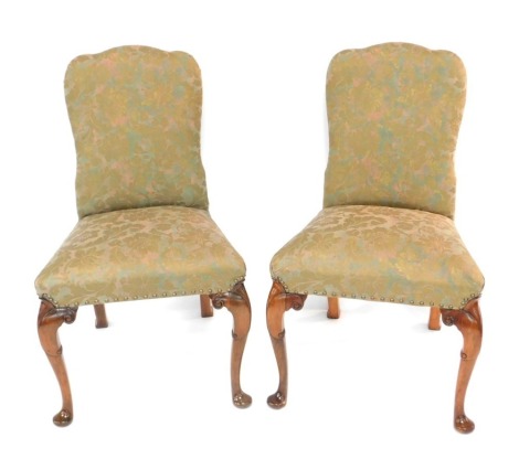 A pair of early 20thC George I style walnut single dining chairs, upholstered in gold floral fabric, raised on carved cabriole legs.