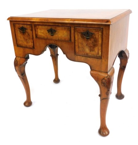 A George I style walnut lowboy, with boxwood strung top, above arrangement of one short and two long drawers, with arched and moulded front, on cabriole shell capped legs, 75cm high, 74cm wide, 51cm deep.