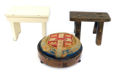 Three stools, comprising a late 19th/early 20thC needlework stool, with shield crested top cushion, on mahogany bun feet, a 19thC elm milking stool and a white painted stool. (3)