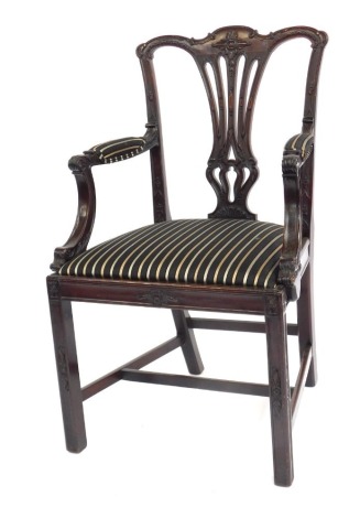 A late 19th/early 20thC mahogany elbow chair, with a carved pierced vase shaped splat, striped fabric arm supports, and drop in seat, on carved channelled legs with H stretcher.