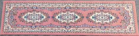 A Chinese wool cut runner, on a pink ground with central floral medallion, 227cm x 59cm.