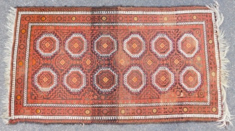 An Eastern rug, on a red ground with four medallions, orange and cream border with tassel ends, 187cm x 106cm.