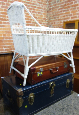 An early 20thC brown leather suitcase, 71cm wide, together with a travelling trunk, and a wicker child's bassinet. (3)