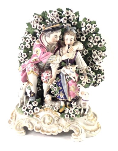 A Continental Derby style porcelain figure group, modelled in the form of a gentleman and lady playing pipes with a lamb, with flowers, etc. on a rococo scroll base, possibly Samson, 24cm high.