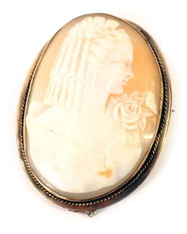 A 19thC shell cameo brooch, depicting maiden looking dexter, with rose design shoulder piece and dress, in a yellow metal rope twist outer framed border, with single pin back and safety chain, 6cm x 4cm, yellow metal unmarked, 16.3g all in.