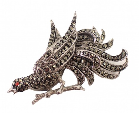 A marcasite bird brooch, perched on a leaf with a red glass eye, in white metal stamped 925, 4cm wide, 10.7g all in.