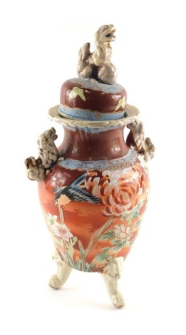 A Japanese earthenware vase and cover, the cover cast with a kylin or dog of fo, the base decorated with pink flowers on a red ground with three scroll cast feet, 40cm high.