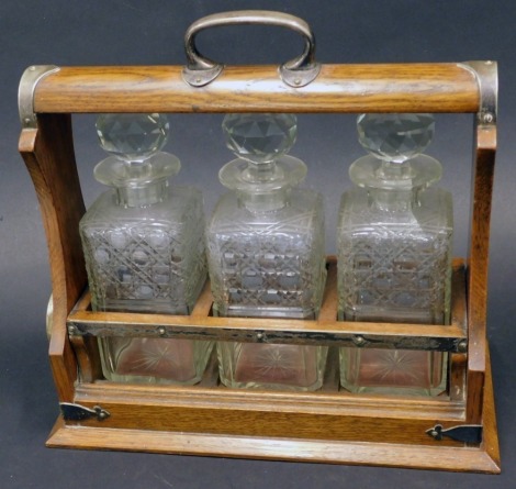 An Edwardian oak and silver plated tantalus, with four cut glass square section decanters and faceted stoppers, with a key, 35cm wide.