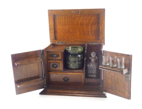 An early 20thC oak smoker's cabinet, with hinged lid and doors, enclosing three drawers, pipe rack, a spirit decanter and stopper, and an associated Portmeirion Totem pattern tobacco jar and cover.