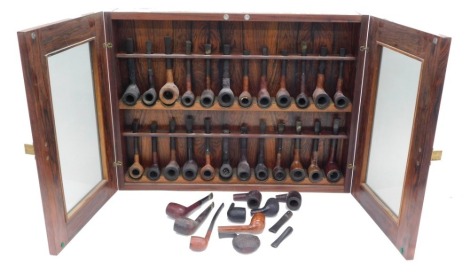 A large collection of briar and other wooden pipes, contained within a rosewood wall cabinet, stamped Lysgaard, Denmark, 60cm wide.