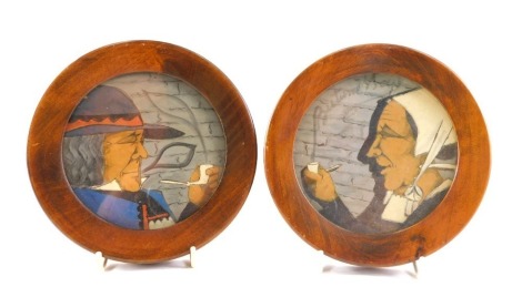 A pair of Paul Fouillen Quimper faience cabinet plates, each carved depicting lady and gentleman smoking, in oak frames, 15cm diameter.