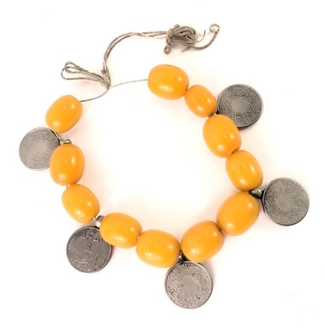 An eastern butterscotch amber bracelet, set with eleven oblong butterscotch amber beads of varying size, the largest 1.5cm wide, on string strand with coin medallion bracelet, 54g all in.