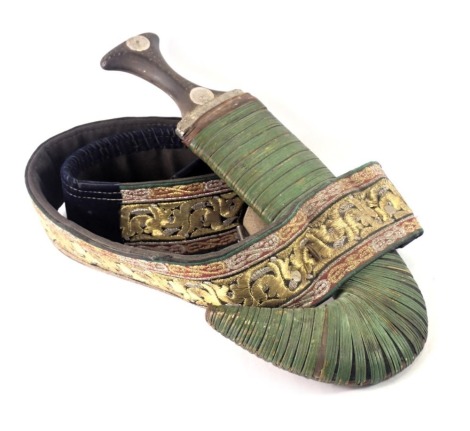 A Middle Eastern short dagger or jambaya, the horn handle embellished with silver coloured metal, brass and copper studs, with leather scabbard and elaborate metallic embroidered belt.