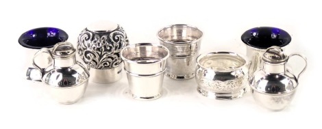 A collection of small silver, to include two beakers, napkin ring, scent bottle lid with cork interior, pair of salts with blue glass liners, and a silver plated cruet modelled as a Jersey Cream jugs. (8)