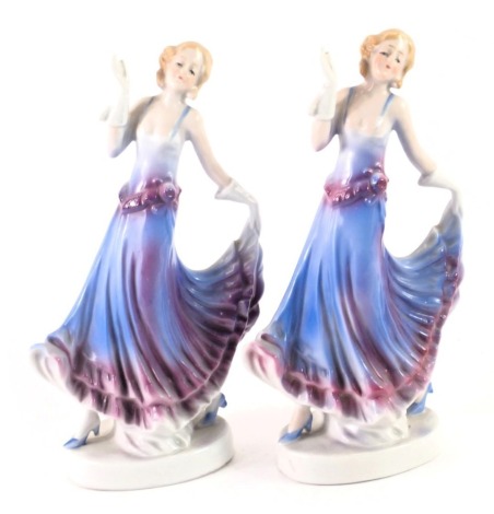 A pair of German porcelain Art Deco style ladies, each in blue and purple flowing gown, on circular foot, numbered 8719, 20cm high.