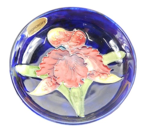 A Moorcroft pin dish, on a blue glazed ground, with hibiscus red flower, 11.5cm diameter, with gold Moorcroft stamp.