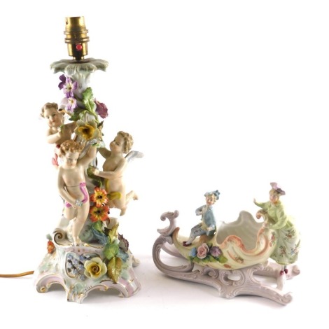 A German porcelain table lamp, modelled with putty, flowers, etc., (AF), 40cm high overall, and a Troika shaped centre piece embellished with two figures, flowers, etc. (2) WARNING! This lot contains untested or unsafe electrical items. It is supplied fo