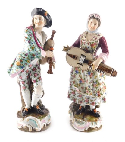 A pair of German porcelain figures, each modelled in the form of a musician, and wearing floral clothing, on a rococo scroll base, 33cm high. (AF)