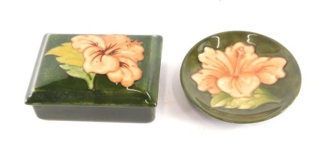 A rectangular Moorcroft box and cover, decorated with a flower, on a green ground, and a matching small dish.