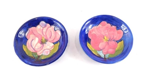 A pair of Moorcroft shallow dishes, each decorated with a large pink flower, on a blue ground, printed marks and hand scripted marks to underside, 18cm diameter.