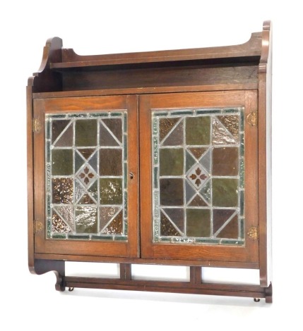 A late 19th/early 20thC oak wall cabinet, the top with a single shelf shaped sides above two stained glass and leaded doors, 96cm high, 77cm wide.