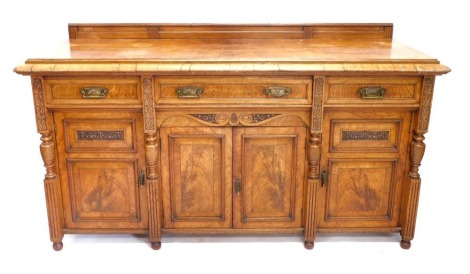 A late Victorian figured oak and oak sideboard, with a later raised back and a moulded edge, above three frieze drawers, each with brass aesthetic style handles, and an arrangement of four panelled doors, flanked by part turned leaf carved and fluted pila