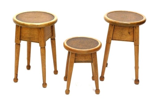 Three oak and beech Arts and Crafts style occasional table, each with a circular top inset with brown leatherette, on turned tapering legs with ball feet, comprising a pair of tables, 45cm high, 29cm diameter, and a smaller example, 33cm high, 26cm diamet