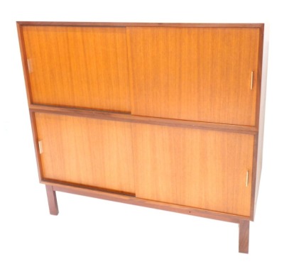 A 1960s/70s Carson teak two section cabinet, each with sliding doors and aluminium handles, on block feet, 118cm high, 122cm wide, 47.5cm deep.